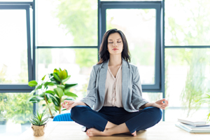 Woman meditating in a lotus position while sitting on her desk.
