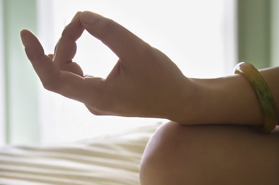 Close up of woman's hand resting on her knee with fingers in meditation pose.