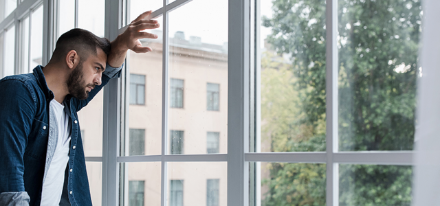Man leaning against windows, looking out anxious